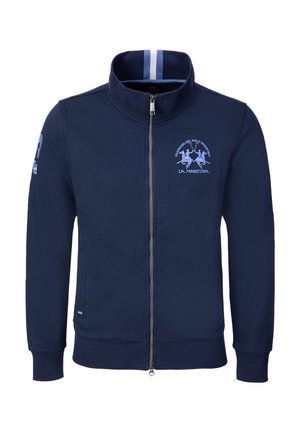 Marineblaue Jacke mit Reißverschluss und hohem Kragen, hellblaues Polo-Spieler-Logo und Text auf der Brust, gestreifter Innenkragen und Patch am linken Ärmel.