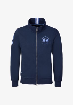 Chaqueta azul marino con cremallera y cuello alto, logo de jugador de polo en azul claro y texto en el pecho, cuello interior a rayas y parche en la manga izquierda.