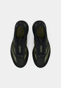 Čierne a olivovo zelené športové topánky s textúrovaným zvrškom, plochými šnúrkami, logom na jazyku a polstrovanou podrážkou.