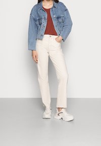 Jeansjacke in Hellblau, rotes Oberteil, cremefarbene gerade Hose und weiße Sneakers mit Leopardenmuster-Akzenten. Einfaches, lässiges Outfit.