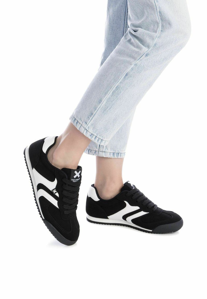 Zapatos deportivos en blanco y negro con parte superior de ante y malla, puntera redondeada, rayas contrastantes, diseño con cordones y suela de goma texturizada.