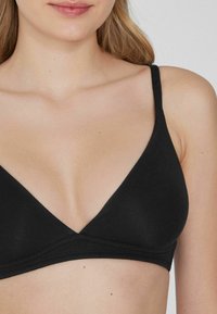 Bralette noir avec un design en V, des bretelles réglables et un tissu doux. Texture lisse et sans couture avec des détails de couture minimalistes.