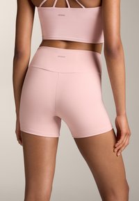Ružové športové šortky s vysokým pásom, vyrobené z hladkého materiálu, s logom na zadnej strane a priliehajúcim strihom.