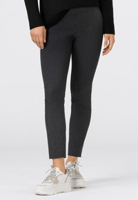 Mörkgrå leggings gjorda av ett elastiskt material, med slim fit och ankellängd, kombinerade med kraftiga vita sneakers.