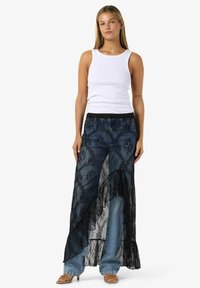 Džínové kalhoty s černou krajkou zdobenou květinovými vzory, nerovným lemem a širokými nohavicemi. Kombinovány s bílým tílkem.
