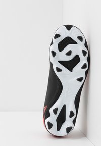 Svart atletisk sko sula med en vit texturerad yttersula som har vinklade utskärningar och en subtil röd accent nära hälen, lättviktsdesign.