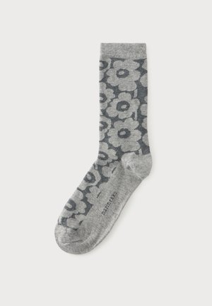 Chaussette grise avec motif floral gris foncé, avec le mot "marimekko" imprimé près des orteils, présentée sur un fond blanc uni.