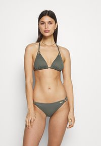 Olive green bikini with triangular top featuring ring accents and adjustable ties, paired with low-rise bottoms also adorned with side hardware.