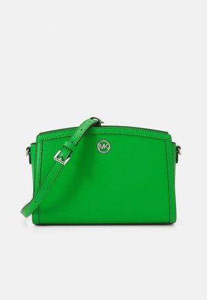 Groene leren crossbodytas met verstelbare band en zilverkleurig rond logo-embleem aan de voorkant in het midden.