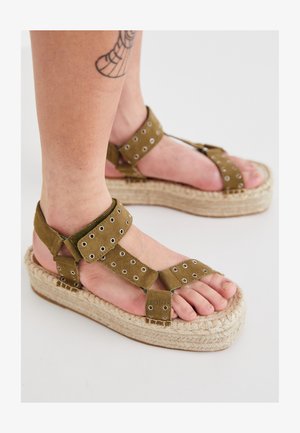Oliivroheline nubukist sandaalid, millel on vitsi disain jute tõmblusega, reguleeritavad rihmad ümmarguste metallist silmadega ja avatud varbad.