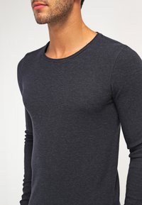 Mörkgrå långärmad tröja med rundad halsringning, som har ett strukturerat tyg och en figurnära design som framhäver ärmarna och överkroppen.