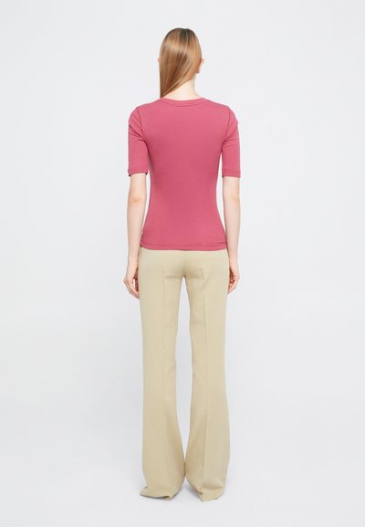 Porcelánrózsaszín, rövid ujjú, környakú felső, világos bézs, bő szárú nadrággal párosítva, minimalista dizájnt bemutatva.