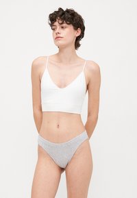 Hvit bralette med tynne stropper, V-halsdesign, kombinert med grå høyt skårne truser, myk tekstur, minimalistisk stil, ingen synlige mønstre.
