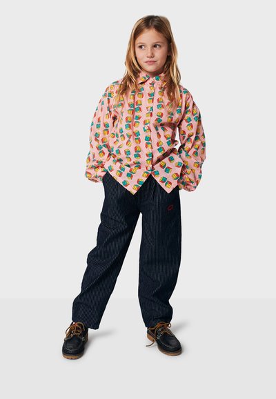 Colorful, patterned shirt with pink base and block designs, paired with dark striped pants. Footwear: black with brown soles and laces.