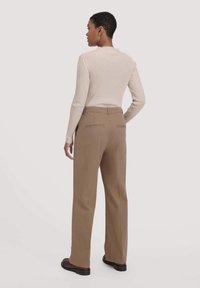 Beige geribbelde trui met een hoge hals en aansluitende mouwen, gecombineerd met lichtbruine broek met wijde pijpen en twee achterzakken.