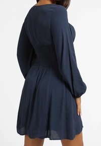 Granatowa sukienka z długimi, bufkowymi rękawami i marszczoną talią, o gładkiej fakturze i rozkloszowanym fasonie, z zamkiem błyskawicznym z tyłu.