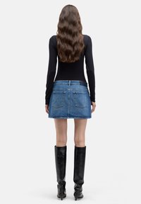 Denim-Minirock mit tailliertem Bund und Gesäßtaschen, kombiniert mit einem schwarzen Langarmtop und kniehohen schwarzen Stiefeln. Glatte Textur.