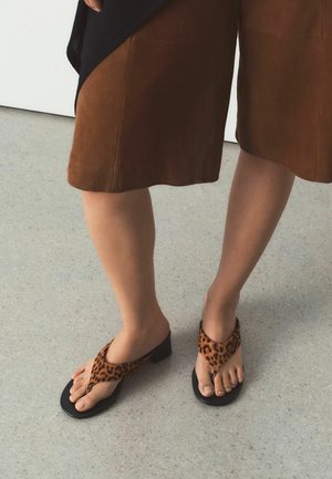 Person trägt braunen knielangen Rock und Leopardenmuster-Absatzsandalen und steht auf grauem Boden.