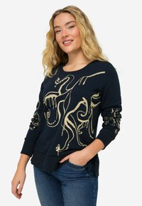 Sweatshirt marine avec un design abstrait doré, col rond, poignets et ourlet côtelés, associé à un jean bleu.