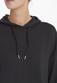 Svart huvtröja i mjukt tyg med en lös passform, med dragsko i huvan och metallagen på dragskorna. Enkelt mönster.