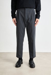 Gray pinstripe trousers with a relaxed fit, featuring a waistband and a straight leg cut. Paired with black shoes and socks.