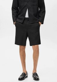 Shorts noirs ajustés en tissu léger, dotés de poches latérales et d'une taille structurée. Associés à une veste assortie et des mocassins.