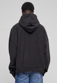 Sort oversized hættebluse med en stor hætte, blød tekstur og drop-skulder, parret med blå jeans med baglommer.