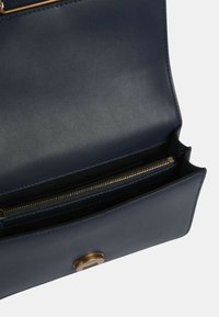 Borsa in pelle blu navy con una superficie liscia, dotata di una cerniera dorata e di un gancio metallico rotondo. All'interno presenta un compartimento con cerniera.