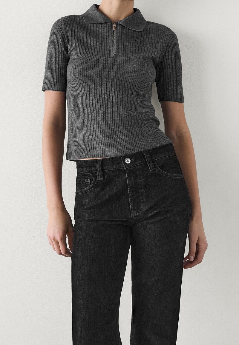 Szary prążkowany top z krótkim rękawem z kołnierzykiem i zamkiem z przodu, zestawiony z czarnymi, wysokim stanem dżinsami z zapięciem na guziki.