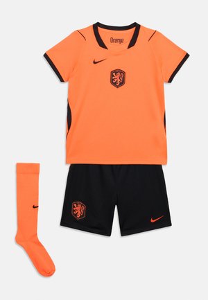 Oranžinė trumpomis rankovėmis futbolo marškinėliai su juoda apdaila, juodi šortai ir oranžinės aukštos kojinės, viskas su „Nike“ logotipais ir KNVB liūto herbu.