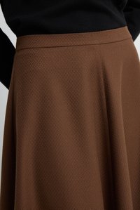 Gonna marrone con una texture, dotata di una cintura liscia e caratterizzata da un sottile motivo geometrico. Il tessuto cade elegantemente con un design svasato.