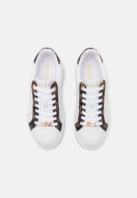 Baskets blanches avec des accents imprimés léopard noirs, côtés texturés, lacets blancs et une plaque logo dorée sur l'avant. Design classique à coupe basse.