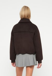 Brązowa krótka kurtka z dużym kołnierzem, teksturowany materiał i elastyczny dół. W zestawieniu z szarą spódnicą plisowaną dla kontrastu.