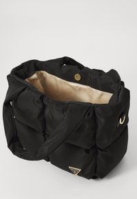 Black nylon tote bag with gathered design, golden triangle logo, and beige interior lining featuring a subtle pattern. Snap closure at top.