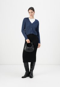 Navy knit cardigan with a cropped design and textured pattern, paired with a fitted black skirt and tall black boots. Holding a black handbag.