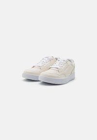 Zapatillas bajas beige hechas de cuero suave con cordones blancos y suelas de goma, con perforaciones y acentos de marca sutiles.