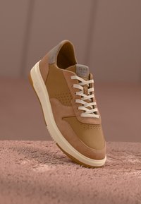 Kreemsuede ja naha tennisjalats valgete paeltega, perforatsioonide ja tekstureeritud kreemja tallaga. Sile ja pehme viimistlus kontrastsete aktsentidega.