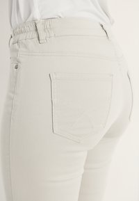 Ljusgrå jeans med en figursydd design, elastisk midja och dekorativ sömnad på bakfickan. Material i bomullsblandning med en slät textur.