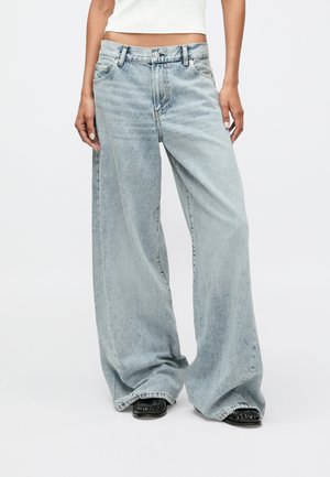 Jasnoniebieskie, szerokie dżinsy wykonane z denimu. Posiadają wysoki stan, pięć kieszeni i subtelny wyblakły wygląd. Widoczne kontrastowe przeszycia.