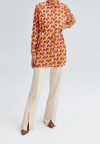 Colorful shirt dress with a geometric pattern in orange, pink, and white, paired with beige wide-leg trousers and brown heels.