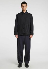 Mustast kangast nööpidega jakk kaeluse ja rinnataskuga. Jaki all on tumesinised püksid ning jalas mustad kingad.