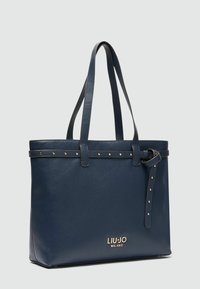 Borsa tote in pelle blu navy con due manici, borchie color oro e dettagli a cintura. Presenta un logo sul fronte. Forma rettangolare, superficie testurizzata.