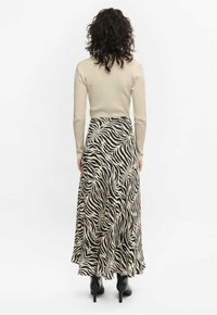 Długa spódnica w print w zebrę w czerni i kremie, zwiewny fason z szerokim dołem, noszona z dopasowaną beżową bluzką z prążkowanego materiału i czarnymi botkami za kostkę.
