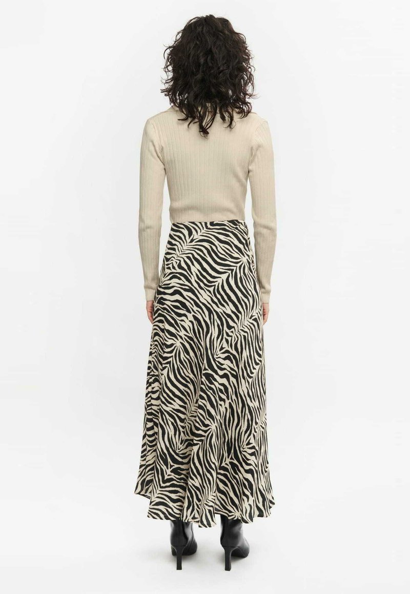 Długa spódnica w print w zebrę w czerni i kremie, zwiewny fason z szerokim dołem, noszona z dopasowaną beżową bluzką z prążkowanego materiału i czarnymi botkami za kostkę.