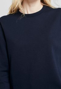 Felpa blu navy, realizzata in tessuto morbido, presenta un collo a giro e maniche lunghe. Texture liscia, design essenziale senza motivi.