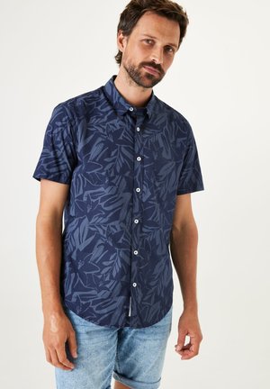 Chemise à manches courtes en bleu marine avec un motif de feuilles ton sur ton, fabriquée en tissu léger, dotée d'un col standard et de cinq boutons.