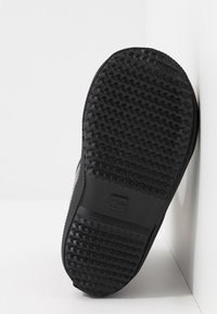 Semelle de chaussure en caoutchouc noir avec un motif texturé. Présente un bout arrondi et un design de semelle standard. Étiquette de taille visible sur le côté.