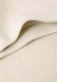 Manta de lana en color beige claro con una superficie suave y texturizada, que presenta un sutil borde doblado y un suave forro interior por debajo.