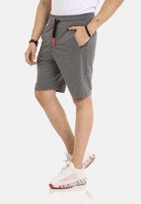 Graue Baumwollshorts mit einem elastischen Bund, schwarzem Kordelzug und Seitentaschen, kombiniert mit weißen und roten Sportschuhen.