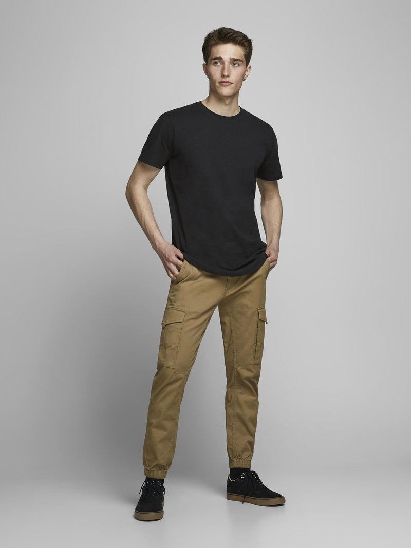 Camiseta negra de manga corta, pantalones cargo beige con bolsillos laterales y zapatillas negras. Corte ajustado con puños en los tobillos ajustables.